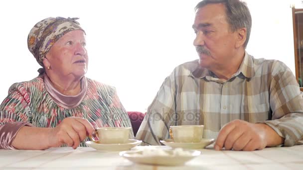 An elderly couple is drinking tea from a vintage Russian kettle samovar. A man with a mustache talking with his wife in a kerchief — Stock Video