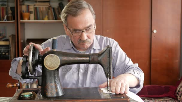 An adult man with a mustache sews on an old hand-sewn machine. Glasses are dressed and white cloth is sewed on. — Stock Video