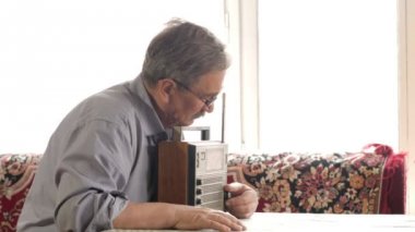 Bıyıklı yaşlı bir adam bir vintage radyoyu ve müzik dinliyor. Anten çeker, üstünde belgili tanımlık düğme döner