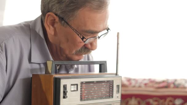 Um homem idoso com bigode liga um rádio vintage e ouve música. Puxa a antena, liga o botão — Vídeo de Stock