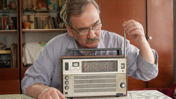 Un anciano con bigote enciende una radio vintage y escucha música. Saca la antena, enciende el botón — Vídeos de Stock