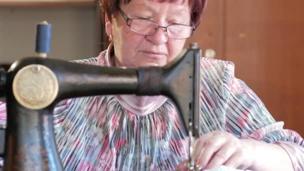 Dorosłej kobiety szyje na starej maszyny do szycia ręcznego. Okulary są ubrani i szary szmatką jest szyte na. — Wideo stockowe