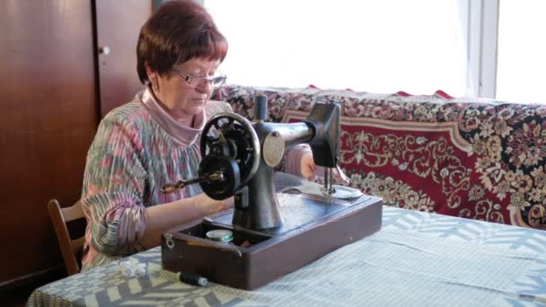 Eine erwachsene Frau näht an der alten Handnähmaschine. Brille angezogen und grauer Stoff aufgenäht. — Stockvideo