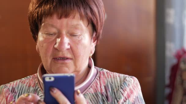 Літня жінка пише текстове повідомлення на мобільному телефоні. Вона обережно натискає на екран і вимовляє текст . — стокове відео