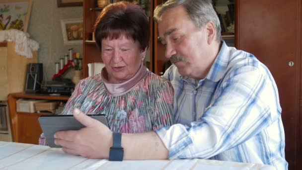 Пожилая пара общается со своим внуком по видео, связывающему планшет. Мужчина и женщина разговаривают с родственниками . — стоковое видео
