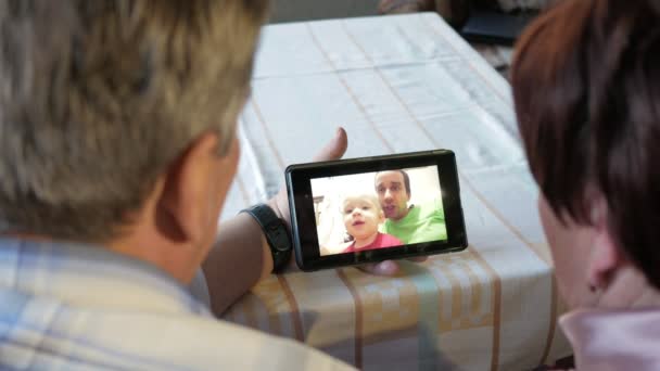 Ein älteres Ehepaar kommuniziert mit seinem Enkelkind per Video, das das Tablet verbindet. Mann und Frau sprechen mit Verwandten. — Stockvideo