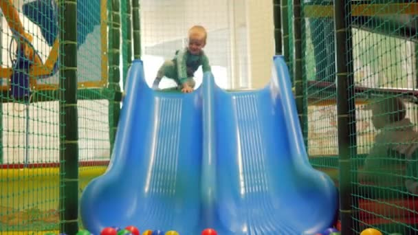 Een schattige jongen trekt uit de blauwe achtbaan in een pretpark. Veelkleurige ballen voldoen aan de jongen — Stockvideo