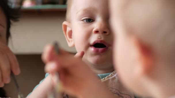 Dos hermanos comen gachas en casa con su madre. Se sientan en una pequeña mesa en casa y comen con una cuchara — Vídeos de Stock