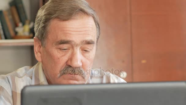 Een oudere man met een snor zit achter een laptop en lost problemen op. Hij kijkt serieus naar de monitor — Stockvideo