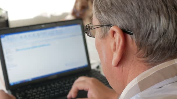 Senior férfi szemüveg működik egy laptop. Úgy néz ki, komolyan, a monitor