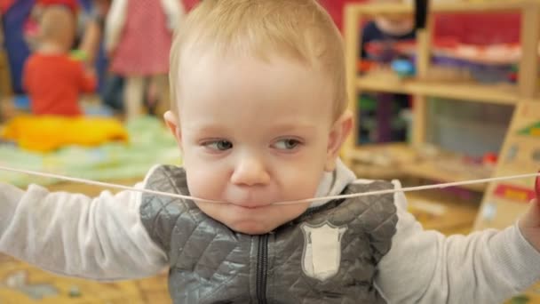 Lindo chico rubio dos años jugando en el centro educativo para niños. El chico está comiendo una cuerda apretada. — Vídeo de stock