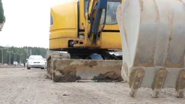 A escavadora fica na estrada com o balde abaixado. Obras rodoviárias são realizadas na cidade — Vídeo de Stock