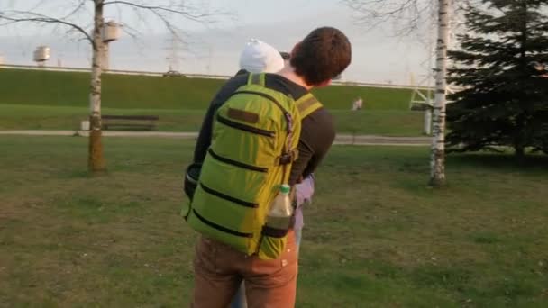 Активная семья с ребенком гуляет в парке весной. Зеленая трава и солнце на закате. Зеленые рюкзаки разных размеров — стоковое видео