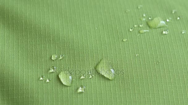 Капли воды падают на зеленую водонепроницаемую ткань рип-стоп. Крупный план — стоковое видео