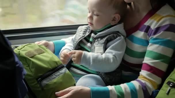 ママは、窓の近く移動の電車の中の赤ちゃんの息子で再生します。少年は母親のひざの上. — ストック動画