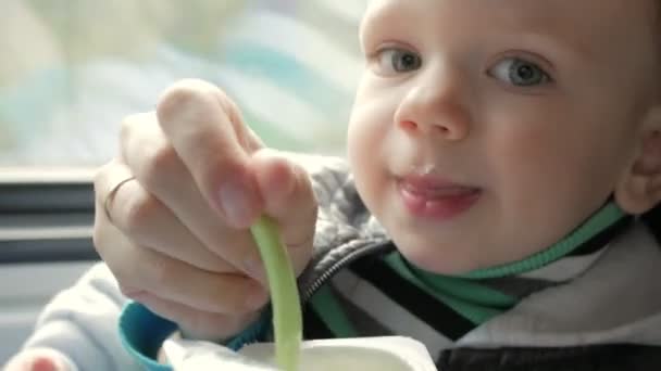 A mãe alimenta o bebé num comboio em movimento perto da janela. Uma colher de plástico a mãe traz mingau de cereal para a boca de seus filhos — Vídeo de Stock