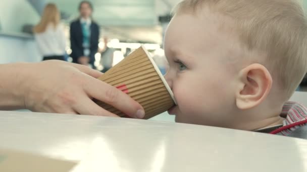 A mãe dá-lhe uma chávena de chá para o aeroporto. O menino desfruta de uma bebida quente em um café — Vídeo de Stock