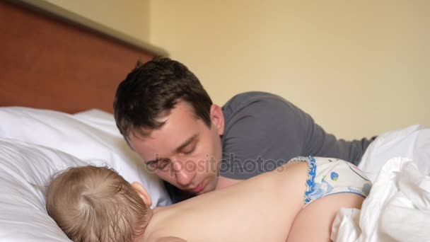 Отец целует сына, который спит в постели. Ребенку меньше двух лет. . — стоковое видео