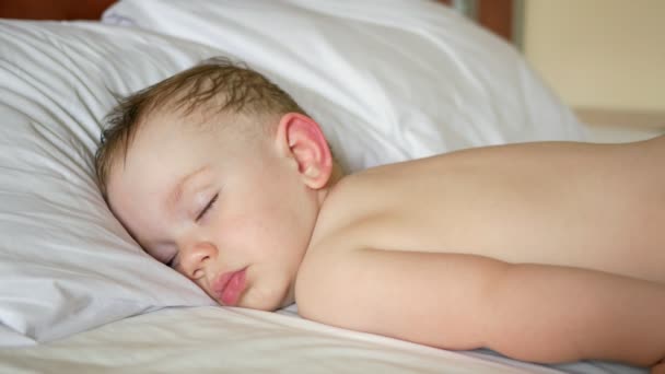 Il bambino dorme su un letto bianco senza camicia. Un po 'di capelli sudati. Primo piano — Video Stock