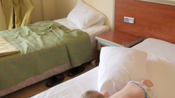 Schattig peuter jongen spelen met kussen op bed en lachen. Hij gooit het en valt ernaast. — Stockvideo