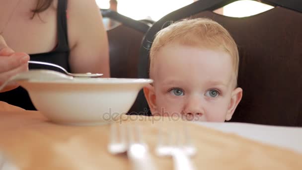 Mamma matar den söt pojken med en matsked café. Blond boy i en grön t-shirt — Stockvideo