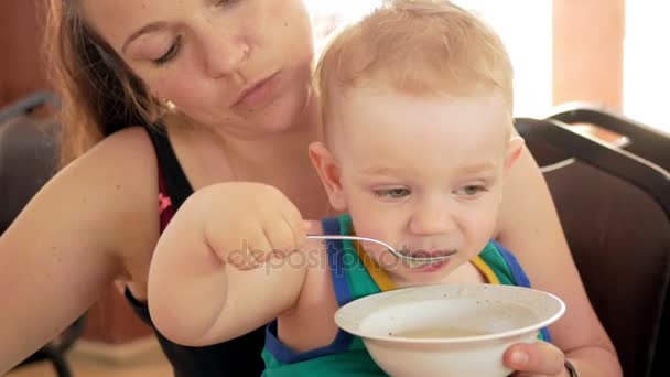 Anne şirin bebek çocuk kafe bir kaşık ile beslenir. Sarışın çocuk yeşil tişört — Stok video
