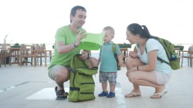 Ebeveynler sırt çantası bir bebek pot al ve bir oğlu koy. Aile deniz kenarında bir lokantada