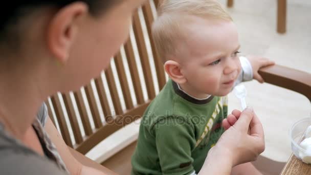 Mère nourrit son jeune fils de crème glacée à partir d'une cuillère. Ils sont assis dans un café de rue. Le garçon aime vraiment la délicatesse . — Video