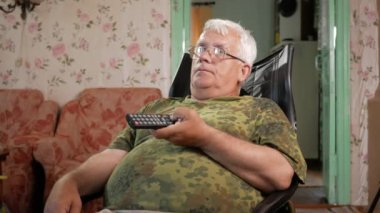 Deri koltukta oturan ve dikkatle televizyon izlerken komuta sizde. Giyinmiş gözlük, gri saç