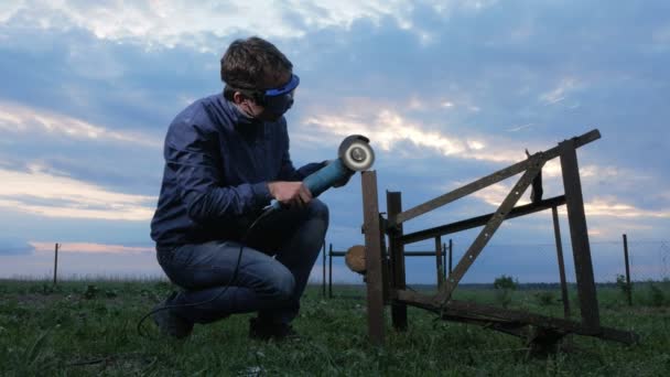 Un joven pule una amoladora angular de metal al atardecer. Hermoso cielo detrás del trabajador . — Vídeos de Stock