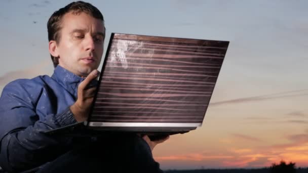 Un joven trabaja detrás de un portátil al atardecer. Hermoso cielo detrás . — Vídeos de Stock