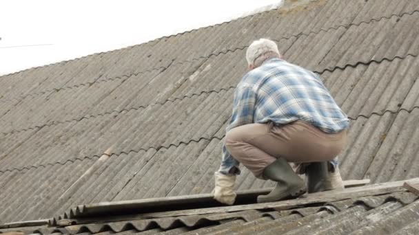 Літній чоловік сам ремонтує дах. Старий дерев'яний будинок у шифері — стокове відео