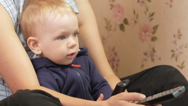 Ung kvinna med sin son som sitter hemma i soffan med fjärrkontrollen från Tv. utseendet på skärmen uppmärksamt — Stockvideo