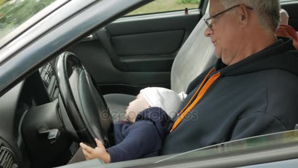 Grand-père joue avec le garçon dans la voiture en conduisant. Le petit-fils est très heureux et tord les différents boutons — Video