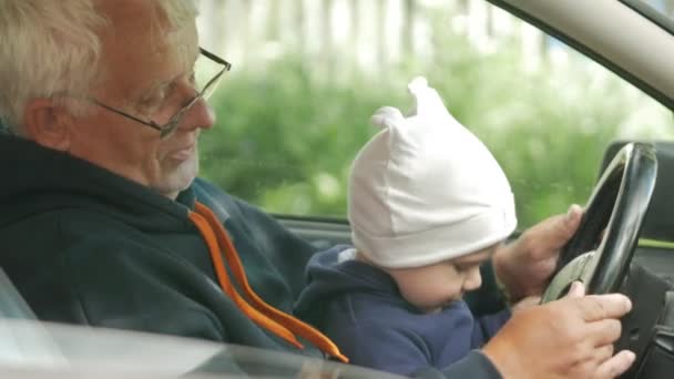 O avô brinca com o rapaz no carro enquanto conduz. O neto está muito feliz e torce os diferentes botões — Vídeo de Stock