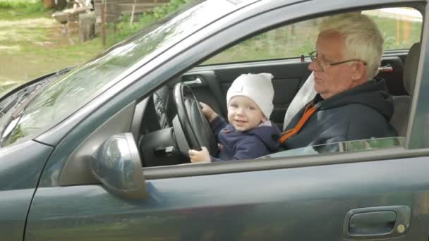 Dziadek bawi chłopiec w samochodzie podczas jazdy. Wnuk jest bardzo szczęśliwy i skręca różne przyciski — Wideo stockowe