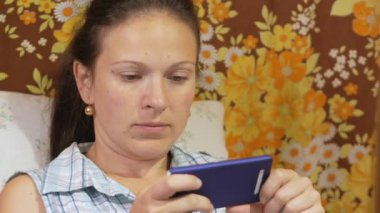 Genç bir kadın cep telefonunuzda ileti bir evde kanepede denetliyor.