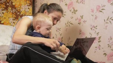 Genç kadın oğluyla evde kanepede oturan ile bir dizüstü bilgisayar. Bakmak dikkatli vasıl belgili tanımlık perde ve belgili tanımlık anahtar taşı tuşuna basın.