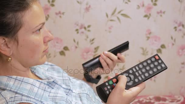 Jovem mulher fica em casa no sofá com casacos da TV. Olha atentamente para a tela — Vídeo de Stock