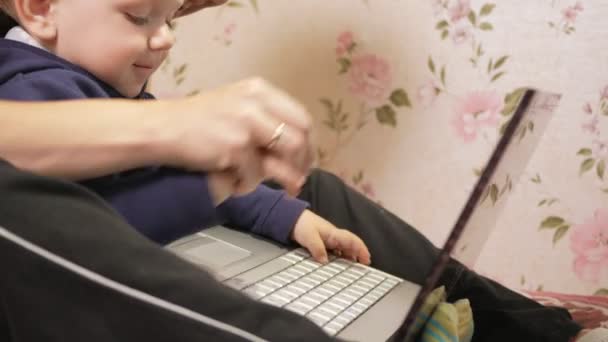 Jonge vrouw met haar zoon om thuis te zitten op de Bank met een laptop. Kijk goed naar het scherm en druk op de toetsen. — Stockvideo