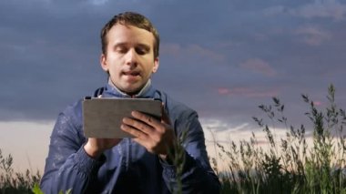 Bir tablet bilgisayarda günbatımında sahada çalışan şirin genç adam. Bir arka plan üzerinde güzel gökyüzü.