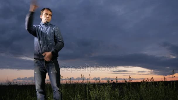 Un giovane uomo carino saluta le zanzare al tramonto sul campo. Bel cielo su uno sfondo . — Video Stock