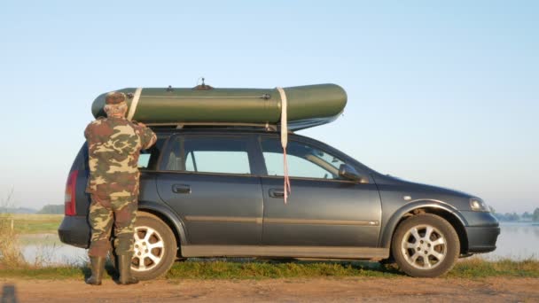 Um homem carrega um barco inflável no telhado do carro para transporte. Fixa com segurança — Vídeo de Stock