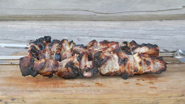 Готовое мясо в барбекю помещается на деревянную доску. Румяные, слегка обгоревшие куски. Деревянные стены на заднем плане — стоковое видео