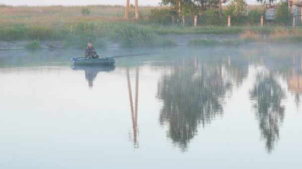 Bateau gonflable avec un pêcheur mâle sur un lac dans le brouillard. Tôt le matin . — Video