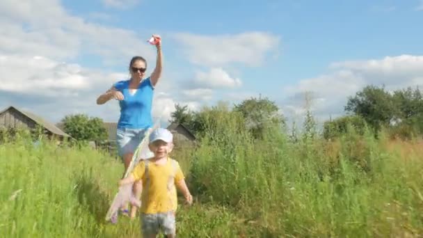 Молодая мать с младенцем запускает воздушного змея в зеленом поле летом. Мама плохо справляется. Сын очень счастлив — стоковое видео