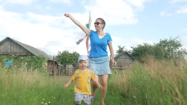 Uma jovem mãe com um bebê lança uma pipa de ar em um campo verde no verão. A mãe não se sai bem. Filho muito feliz — Vídeo de Stock