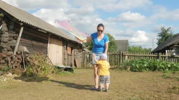 Молодая мать с младенцем запускает воздушного змея в зеленом поле летом. Мама плохо справляется. Сын очень счастлив — стоковое видео
