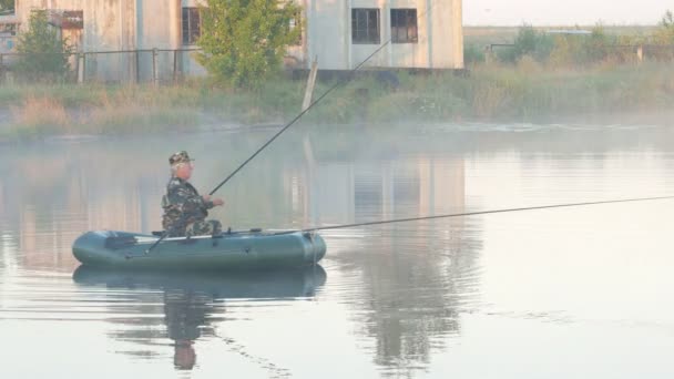 Felfújható csónak, egy férfi halász a tó a ködben. Kora reggel. — Stock videók