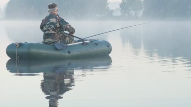 Barco inflable con un pescador masculino en un lago en la niebla. Temprano. . — Vídeos de Stock